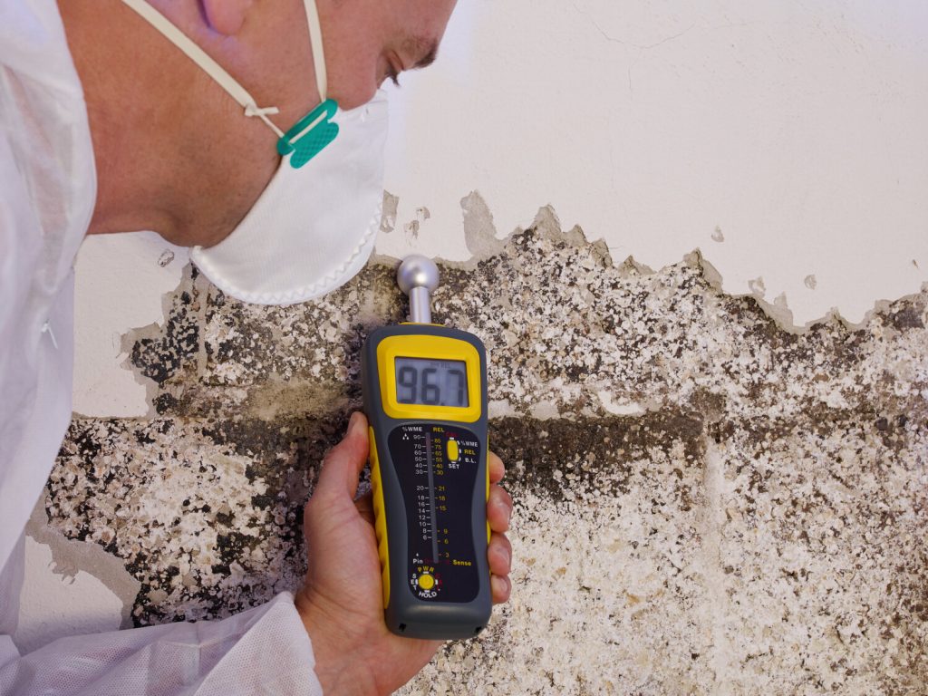 Man wearing a mask while holding a thermal device on a wall