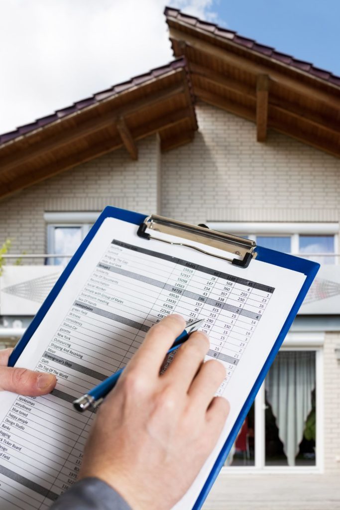 Hands holding a house inspection report form and blue ballpen