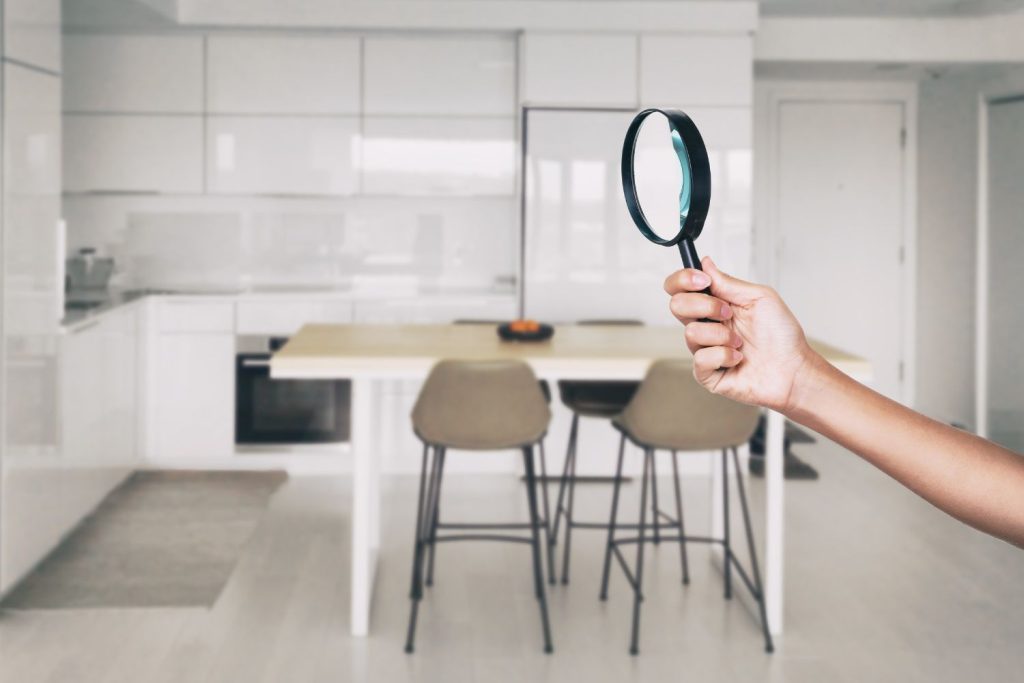 A hand holding a black magnifying glass with the kitchen and dining area background